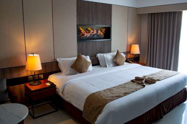 A cozy hotel room with a large bed, two lamps, a decorative headboard, and curtains drawn over the window.