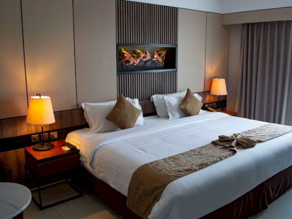 A cozy hotel room with a large bed, two lamps, a decorative headboard, and curtains drawn over the window.
