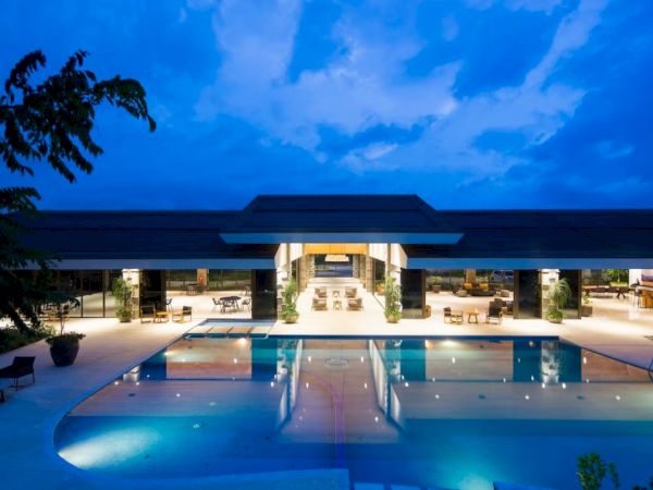 A modern building with open areas, surrounded by a large swimming pool, lit at dusk, creating a serene and inviting ambiance.