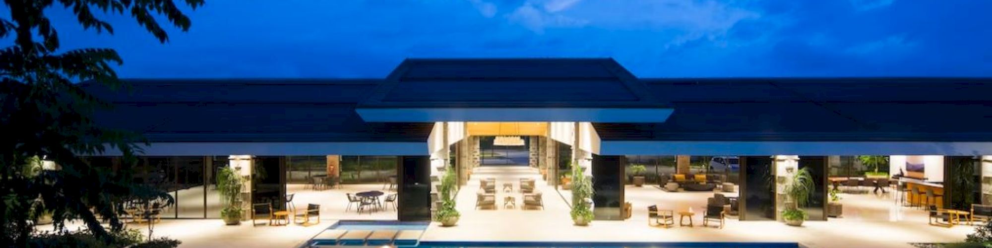 A luxurious poolside area with modern architecture and outdoor seating, set against a twilight sky.