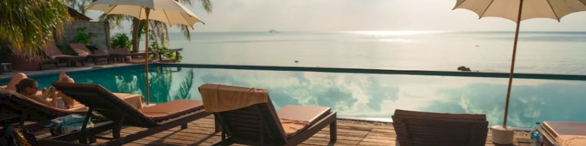 A serene poolside scene with lounge chairs, umbrellas, and a view of the ocean under a partly cloudy sky.