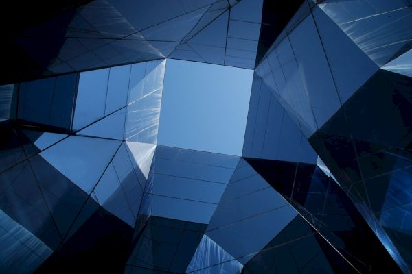 Geometric shapes and reflective surfaces frame a clear view of the blue sky, creating a modern architectural abstract composition.