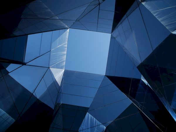 Geometric shapes and reflective surfaces frame a clear view of the blue sky, creating a modern architectural abstract composition.