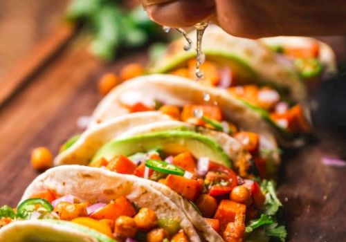 Tacos filled with chickpeas, avocado, and veggies, placed on a board with lime being squeezed over them.