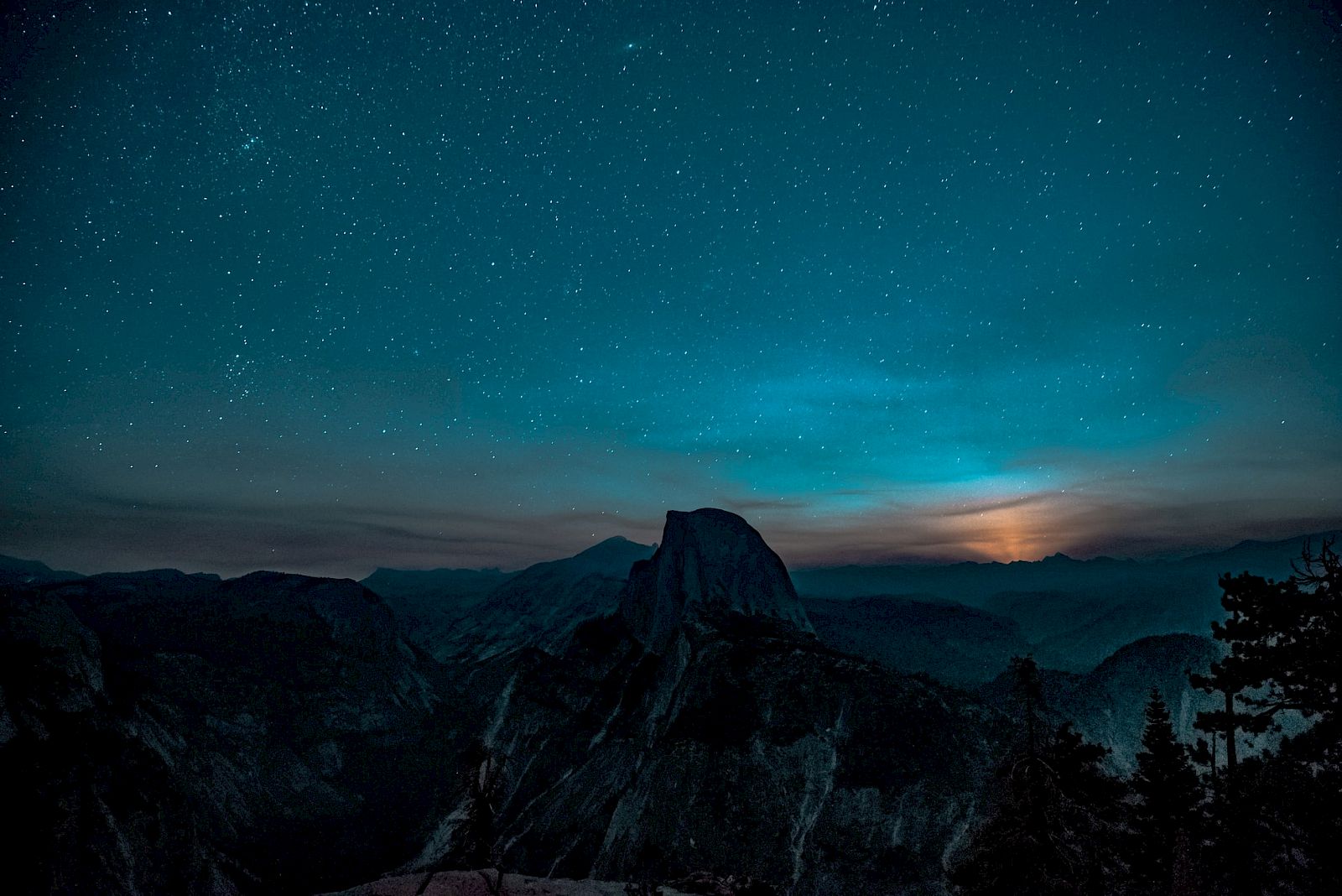 A night sky filled with stars over a mountainous landscape, with a glowing horizon creating a serene and picturesque scene.