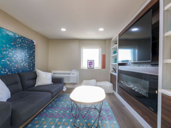 A cozy living room with a dark sofa, colorful rug, large TV, and wall art, featuring modern furniture and decor elements.
