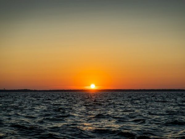 A vibrant sunset over a calm ocean, with the sun touching the horizon and creating a warm glow across the sky and sea.