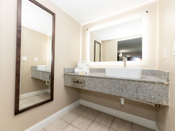 A modern bathroom with a large mirror, granite countertop, vessel sink, and folded towels on the counter.