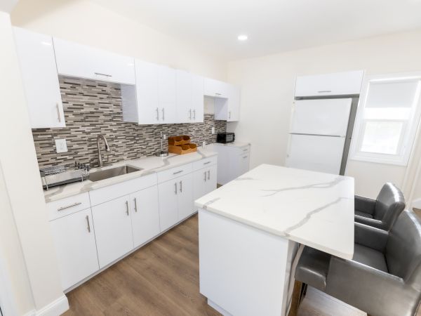 A modern kitchen with white cabinets, a mosaic tile backsplash, a marble island, and grey chairs.