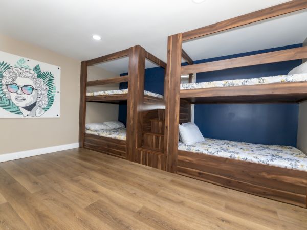 The image shows a room with two wooden bunk beds and a colorful wall art of a person with sunglasses and an abstract leaf background.