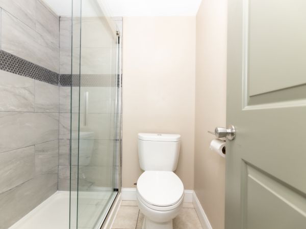 A bathroom featuring a toilet, glass shower door, tiled wall with a decorative band, and a wall-mounted toilet paper holder.