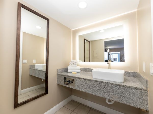 Modern bathroom with large mirror, floating countertop, rectangular sink, and folded towels. Soft lighting creates a clean atmosphere.
