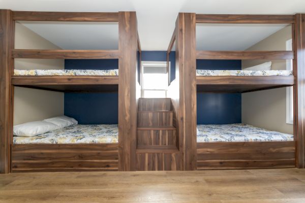 Four wooden bunk beds with a staircase in the center and floral bedding in a room with wood flooring.