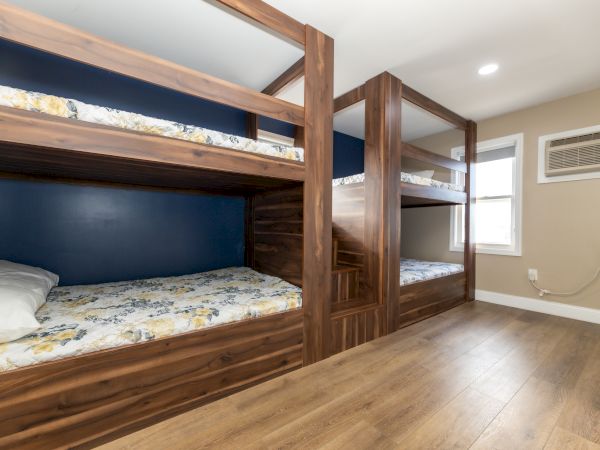 The image shows a room with two sets of wooden bunk beds, a floral-patterned mattress, and an air conditioner on the wall.