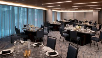 The image shows an elegantly set banquet hall with round tables, black chairs, glassware, and floral centerpieces.