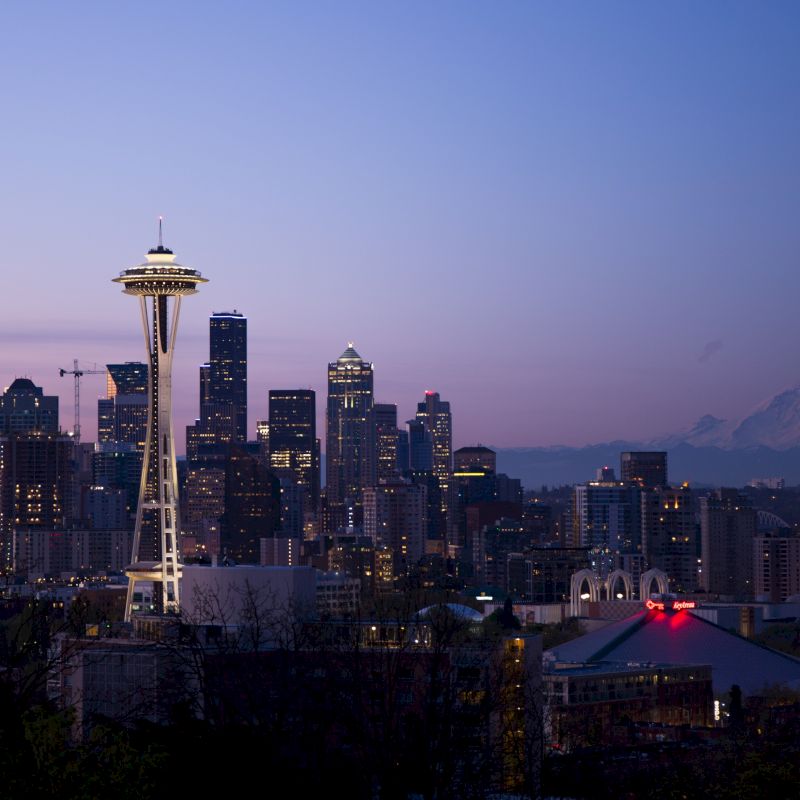 Seattle skyline at dusk with the Space Needle and Mount Rainier in the background against a purple sky.