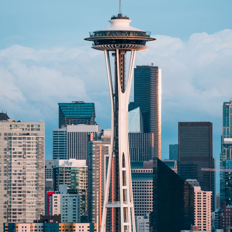 The image shows a city skyline featuring a tall, distinctive tower with a circular top, surrounded by various skyscrapers under a blue sky.
