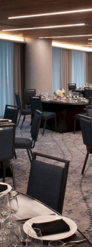 The image shows an elegantly set banquet hall with round tables, wine glasses, and dim lighting, ready for an event or dinner.