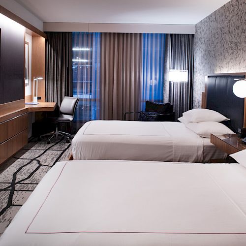The image shows a modern hotel room with two beds, a desk, a TV, and patterned wallpaper, featuring a minimalist design.
